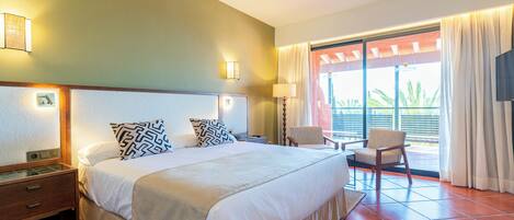 A hotel room with a large bed, a nightstand, a chair, and a view of the outdoors.