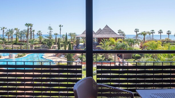 Vue sur un complexe hôtelier avec une piscine, des palmiers et une plage.