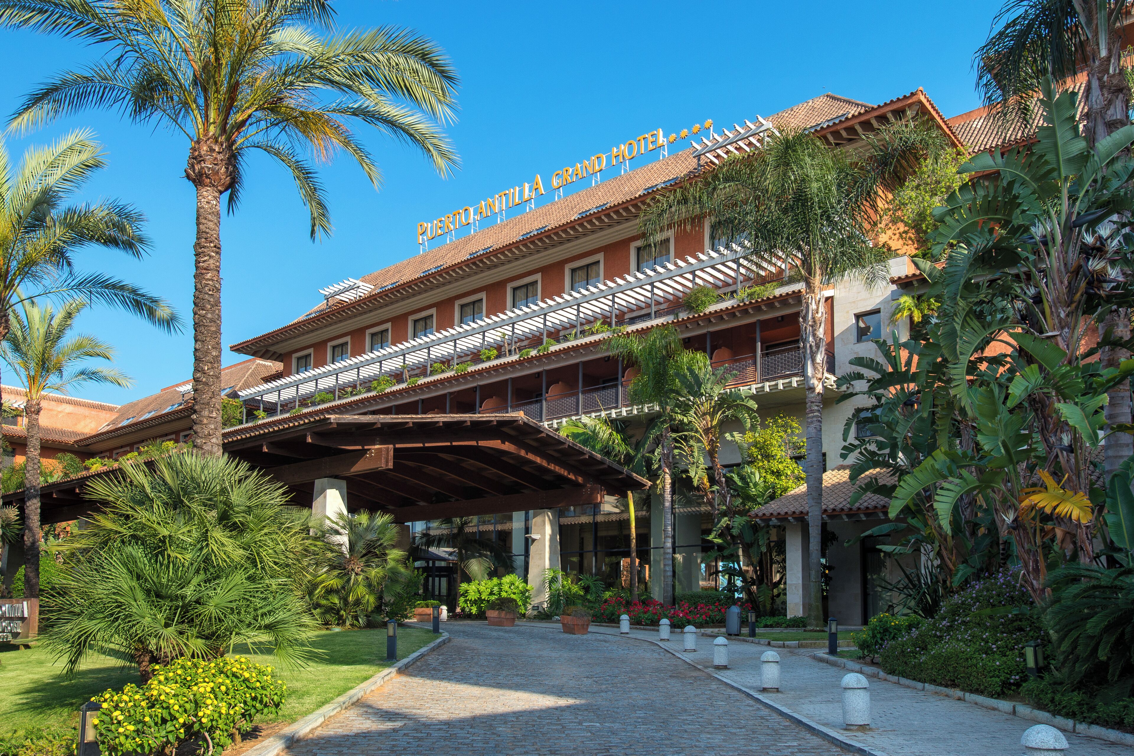 The Puerto Antilla Grand Hotel with a covered entrance, palm trees, and a clear blue sky.