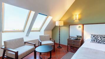 Een hotelkamer met een bed, twee fauteuils, een tafeltje, een nachtkastje, een lamp en uitzicht door dakramen.