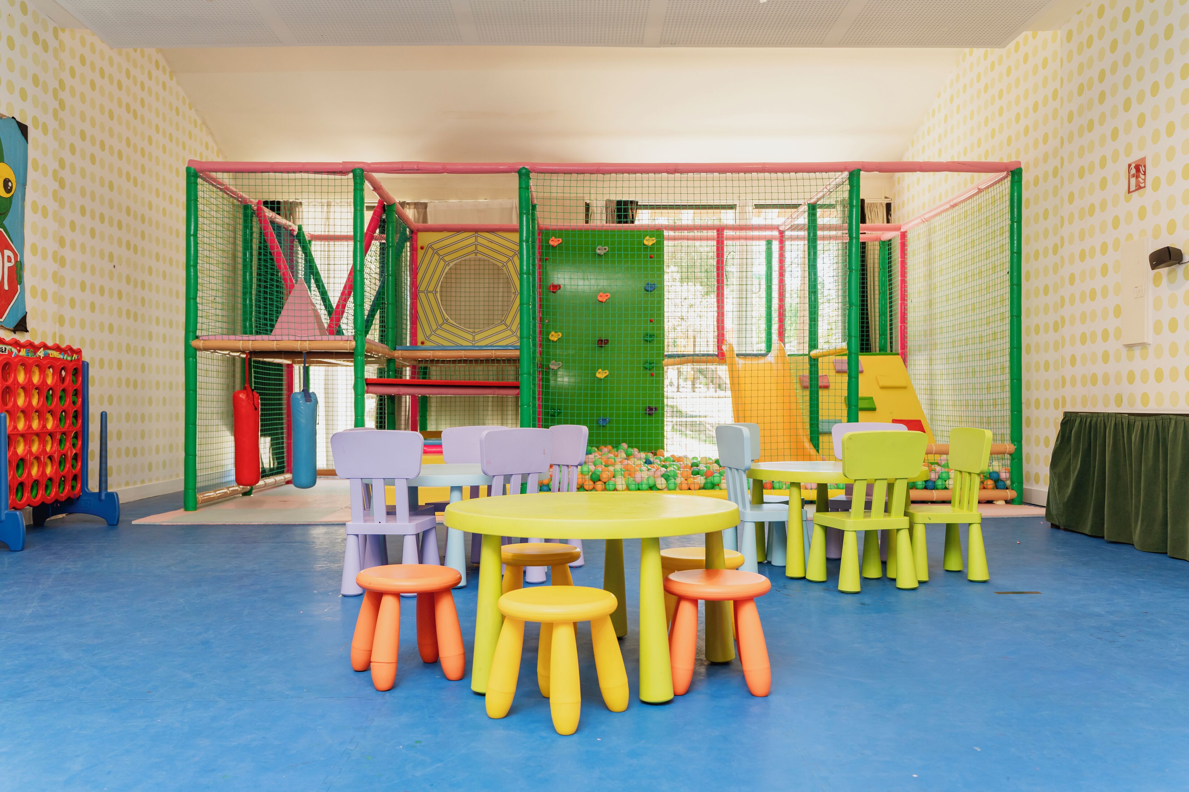 A children's play area with colorful play structures, a table with chairs, and stools.