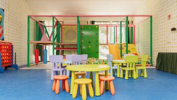 A children's play area with colorful play structures, a table with chairs, and stools.