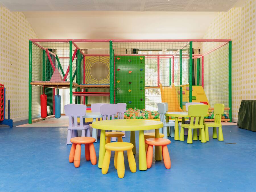 A children's play area with colorful play structures, a table with chairs, and stools.