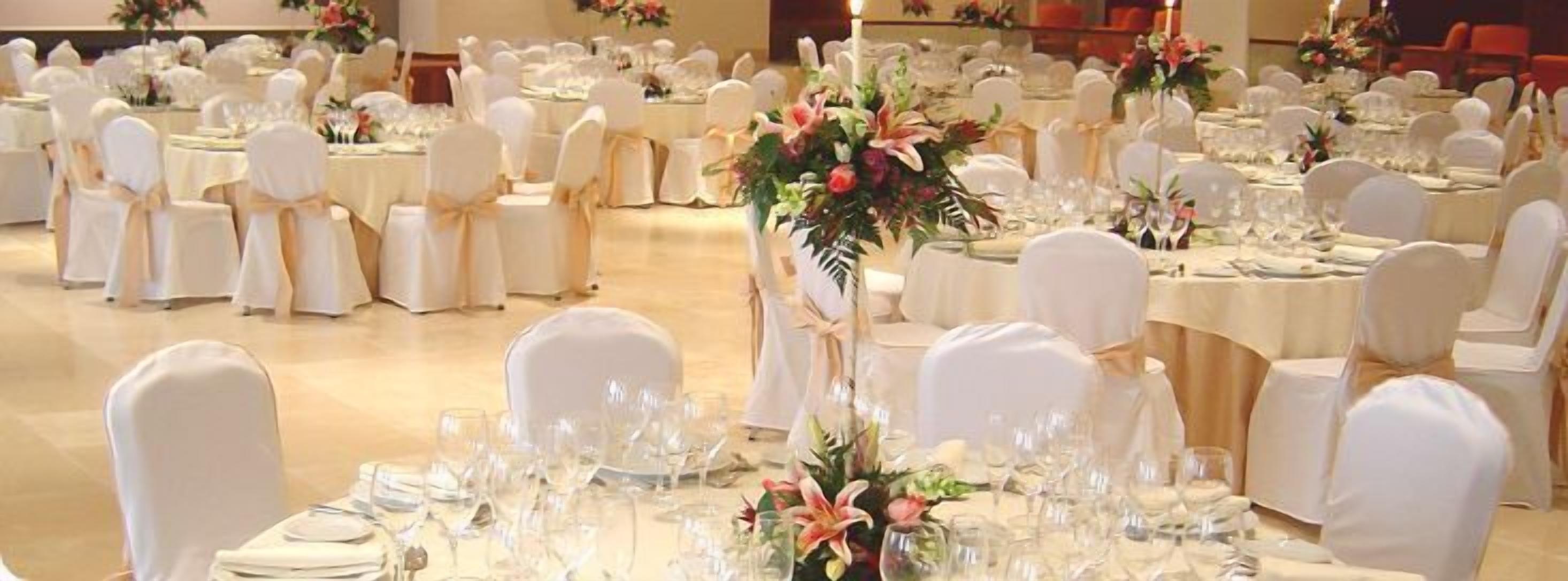 A banquet hall with round tables set for a formal event, each with white tablecloths and floral centerpieces.