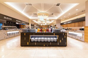 Un área de desayuno moderna con una barra central que exhibe alimentos para el desayuno y una variedad de platos y tazones.