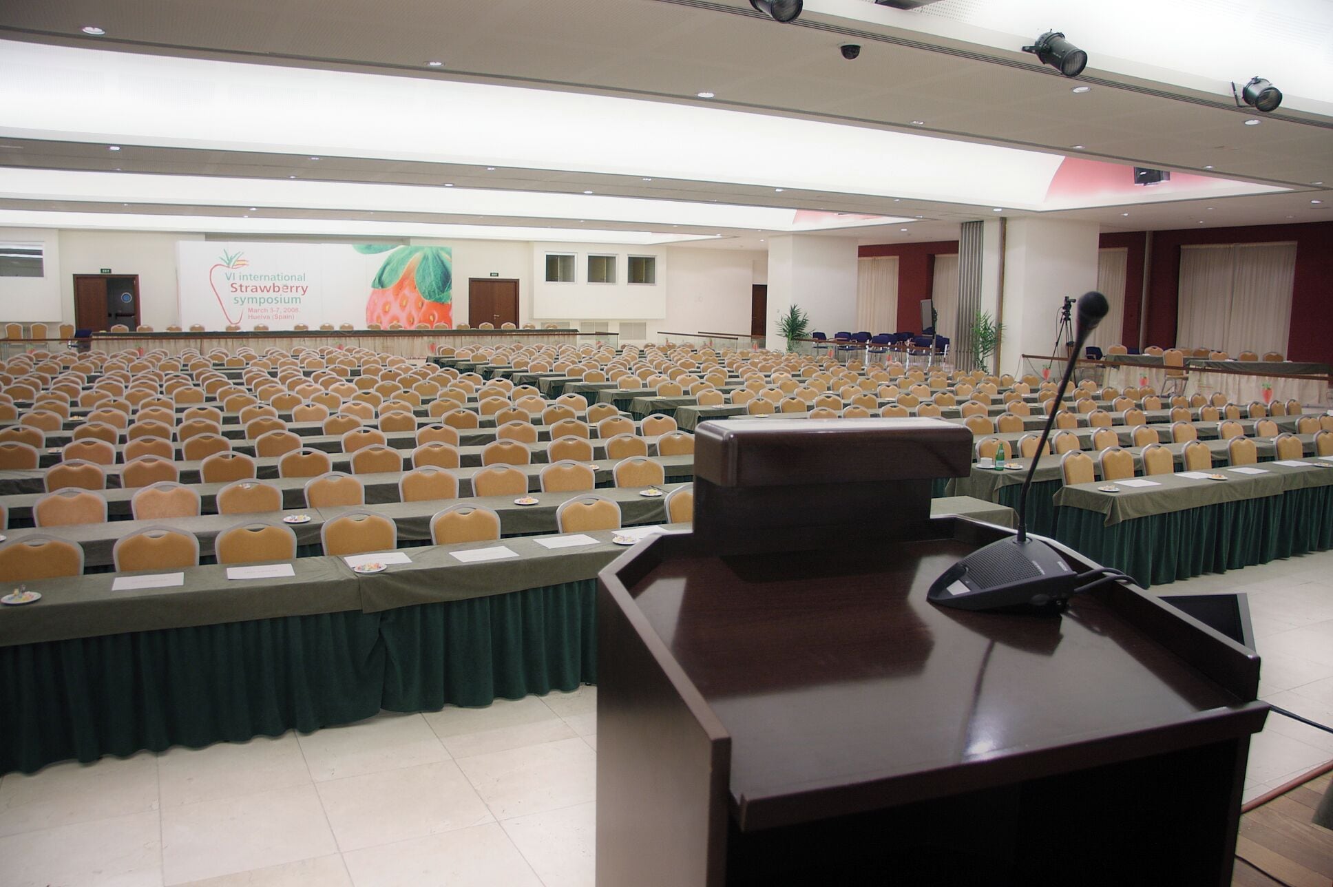 Una sala conferenze con file di sedie, un podio e un grande schermo che mostra uno striscione a tema fragola.