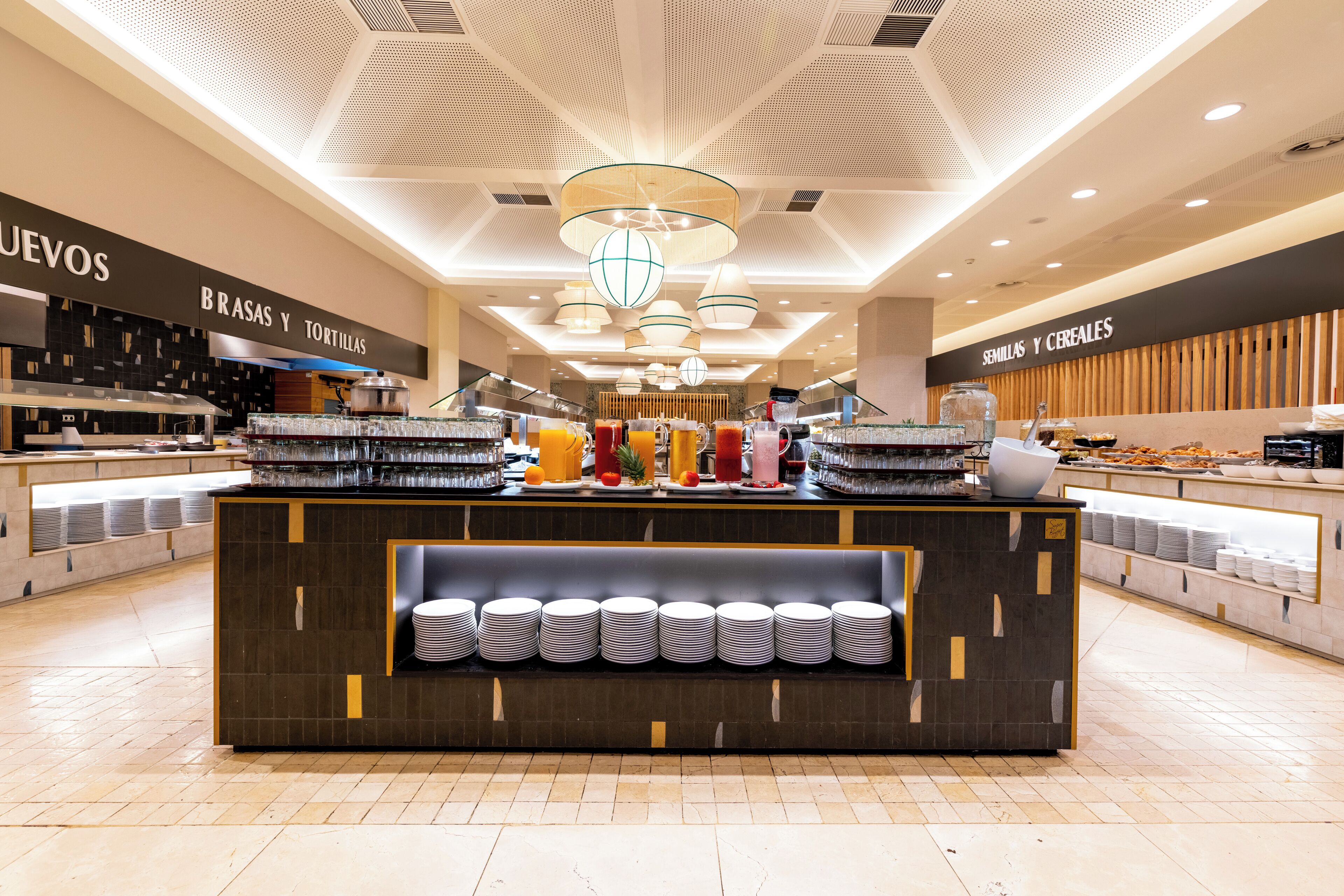 A modern breakfast bar with a central serving area, surrounded by shelves of plates and bowls, and a variety of beverages.