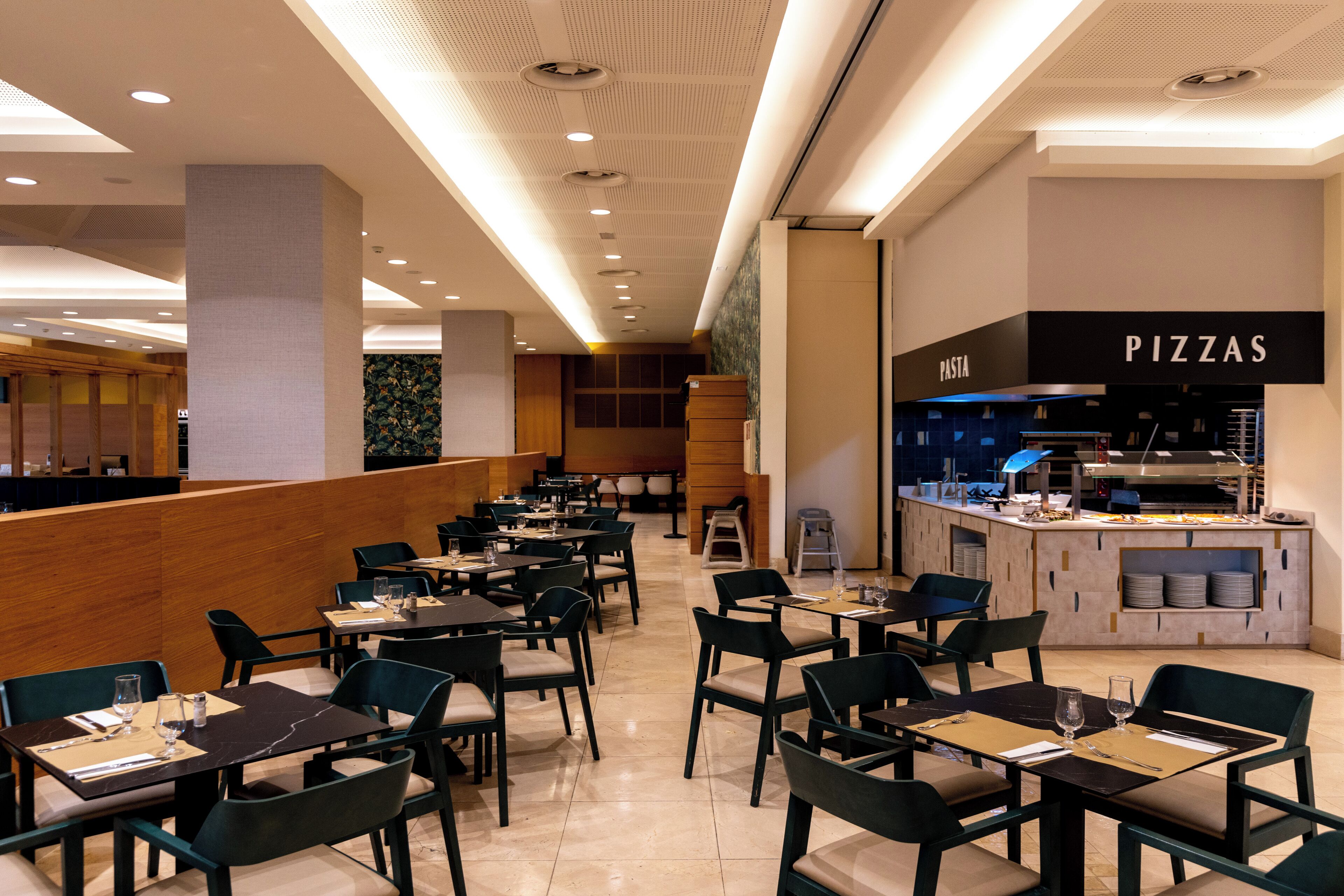 Un restaurante moderno con una barra de pizza, varias mesas y sillas.