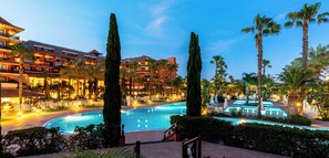 Un hotel con piscina, palmeras y un espacio exterior bien iluminado.