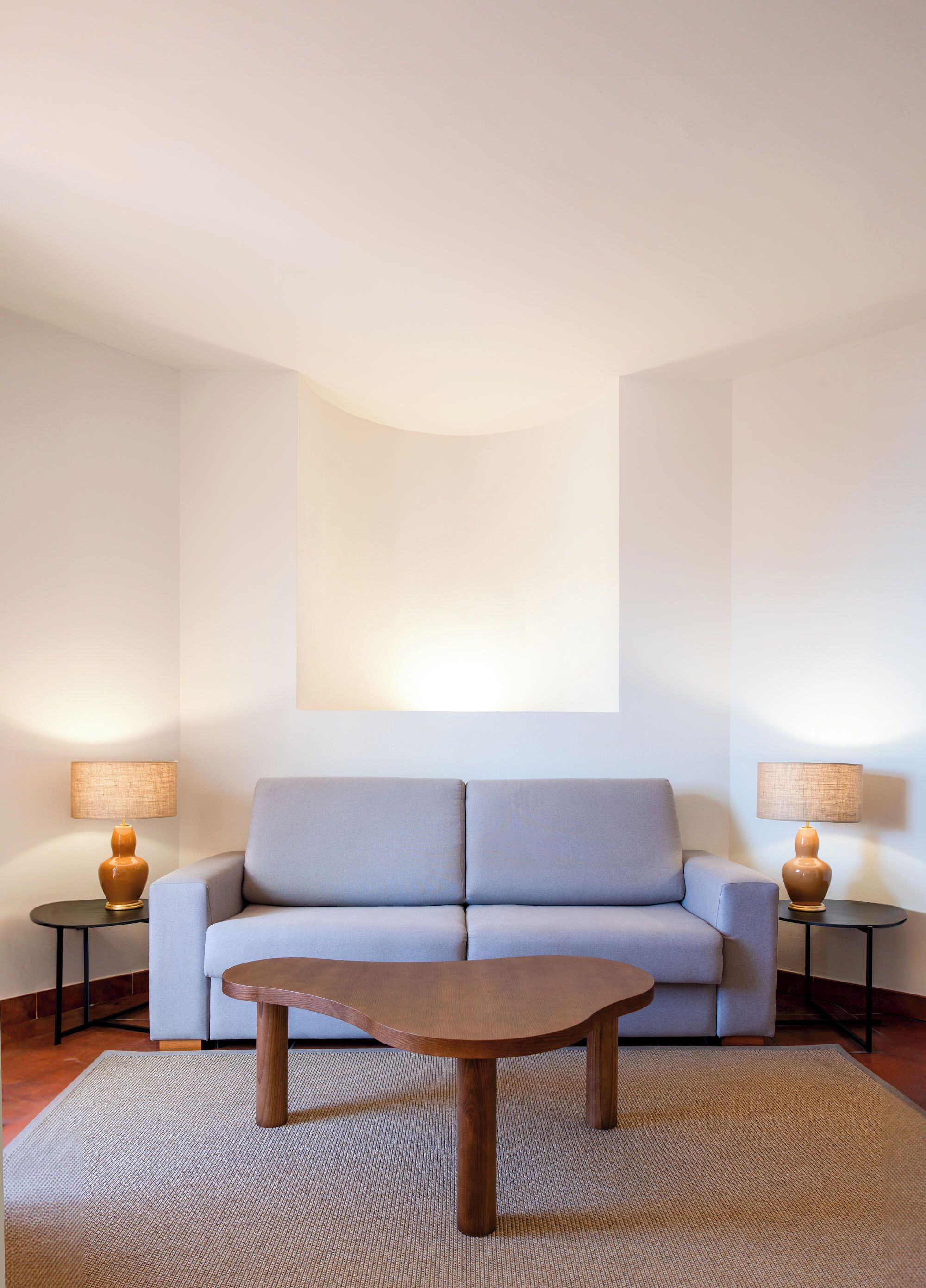 A modern living room with a light blue sofa, a wooden coffee table, and two side tables with lamps.