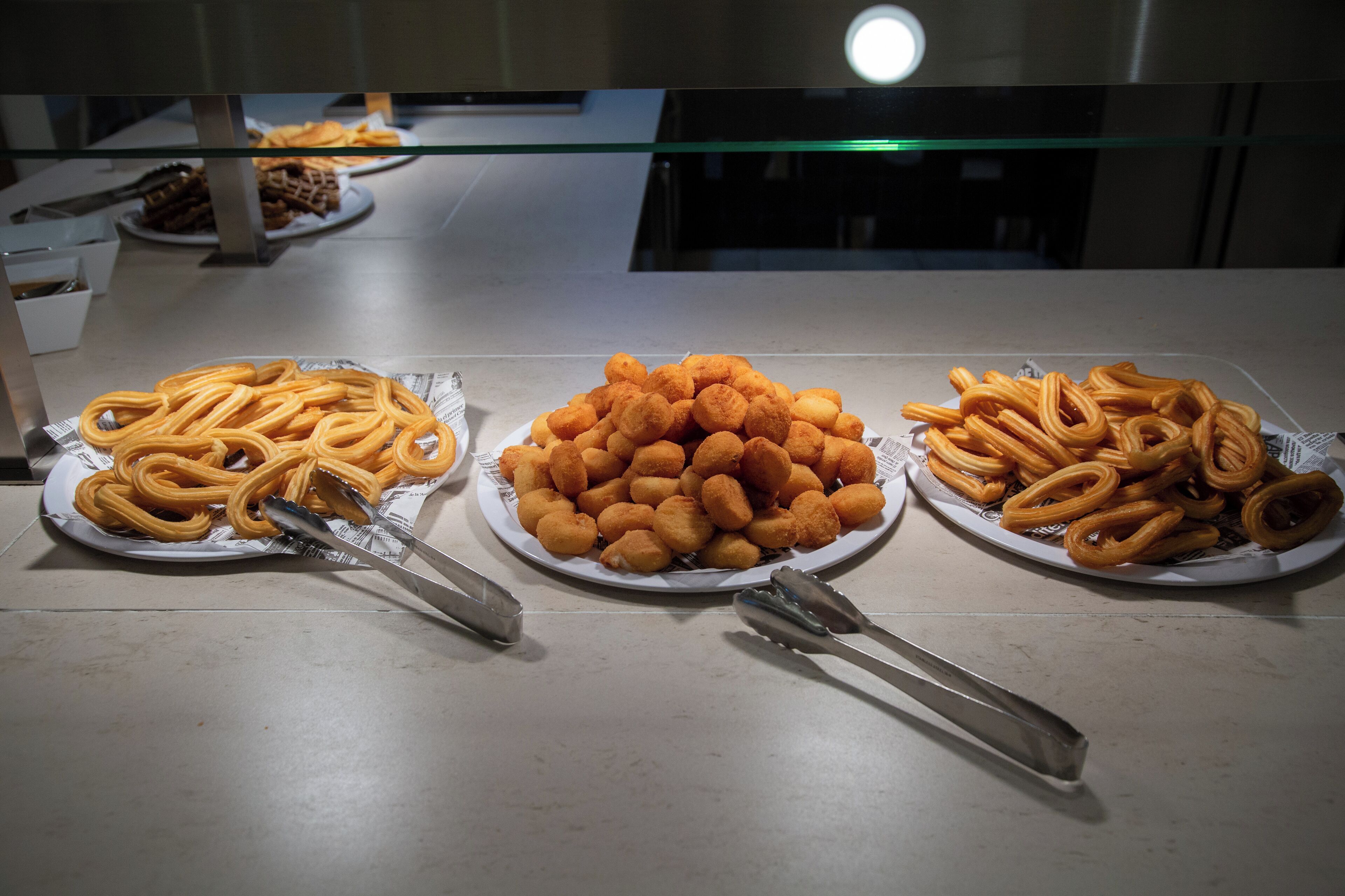 Tres platos de aperitivos de masa frita sobre una mesa, con unas pinzas.