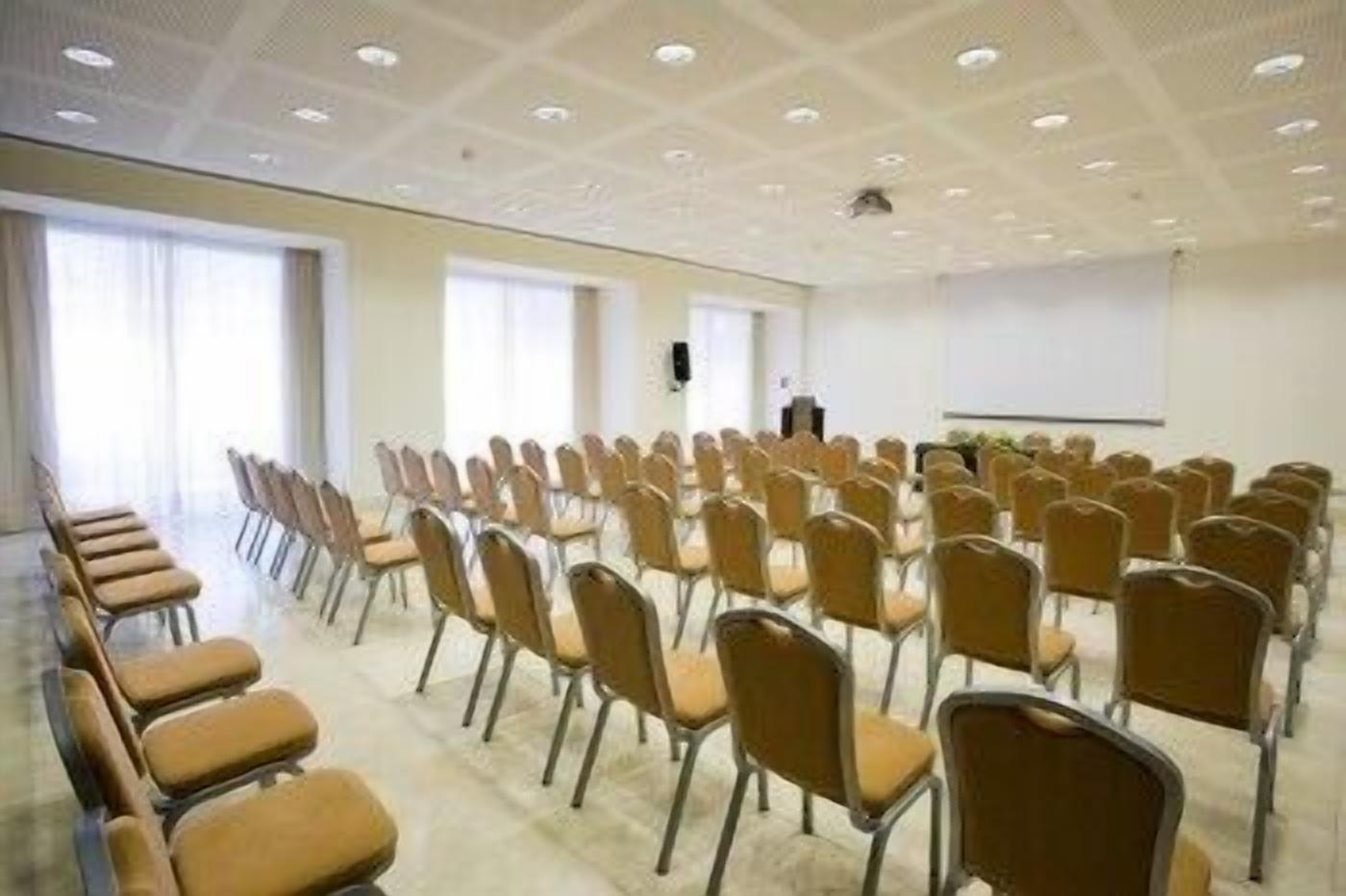 A conference room with rows of chairs, a projector screen, and a speaker's podium.