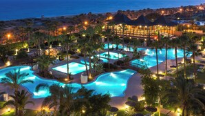 Een resort met meerdere zwembaden, palmbomen en uitzicht op het strand.