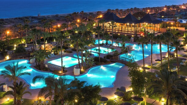 A resort with multiple swimming pools, palm trees, and a beach view.