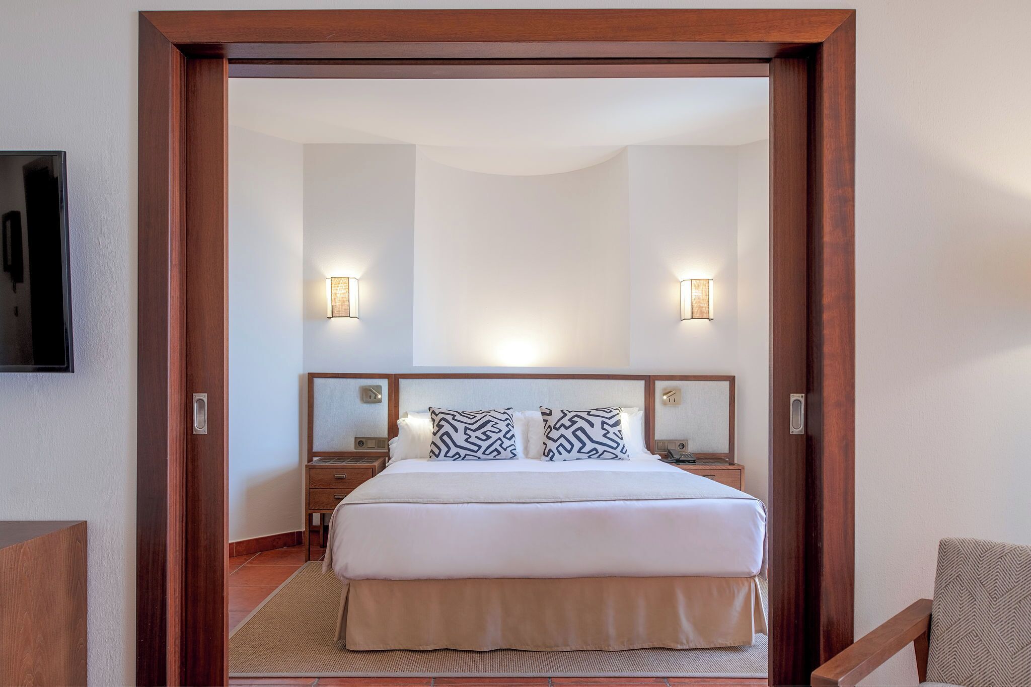 A hotel room with a large bed, two bedside tables, and a mirror above the bed.