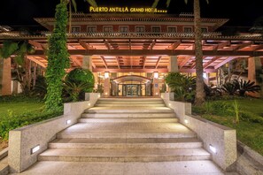 Imponente entrada de hotel con una escalinata de piedra que conduce a un porche cubierto, rodeada de vegetación.