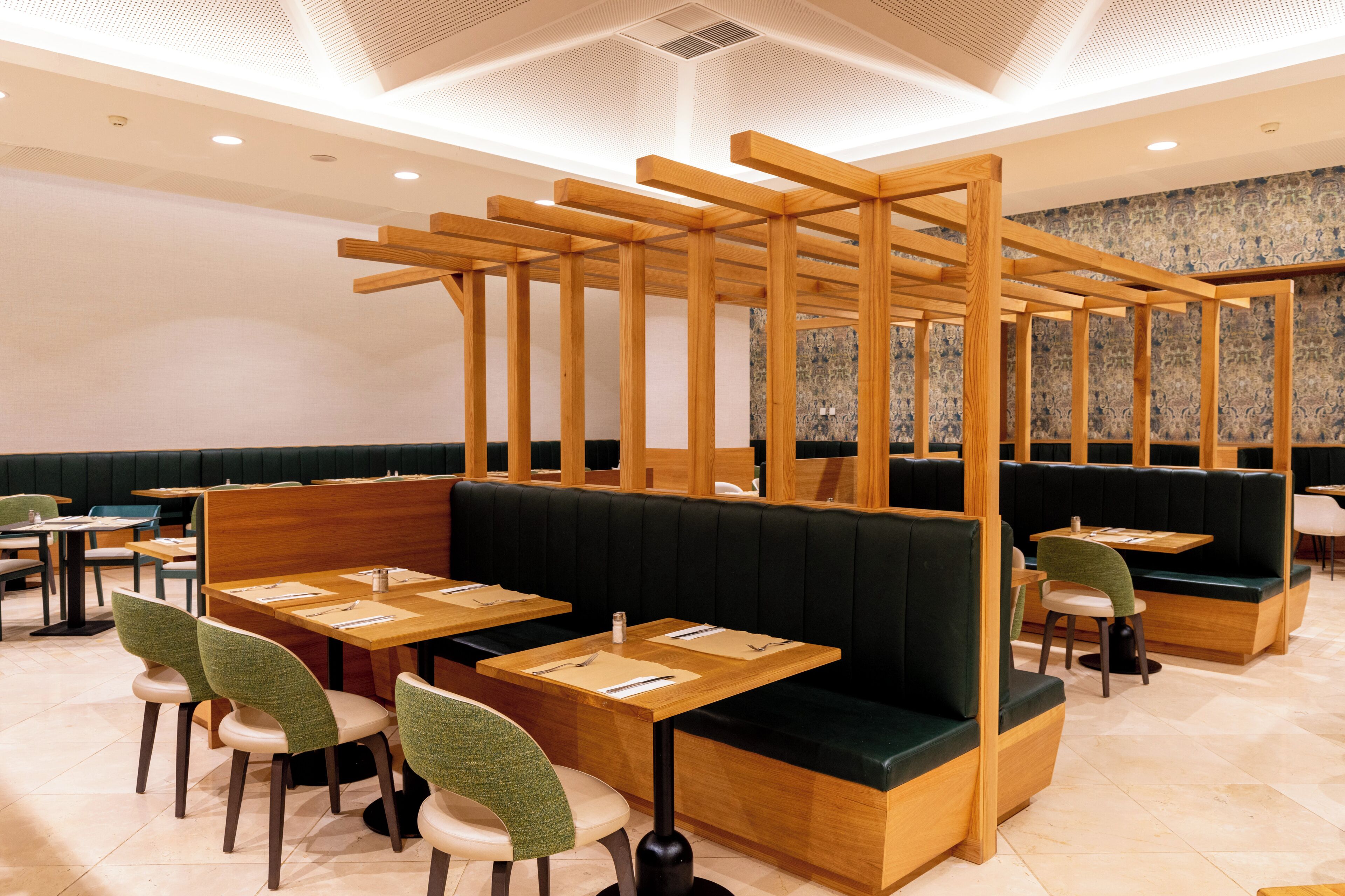 Un restaurante con cabinas de madera, asientos tapizados en verde y una pared con diseño de fondo.