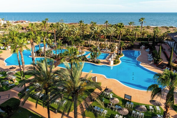 Un resort con varias piscinas, palmeras y vista al mar.