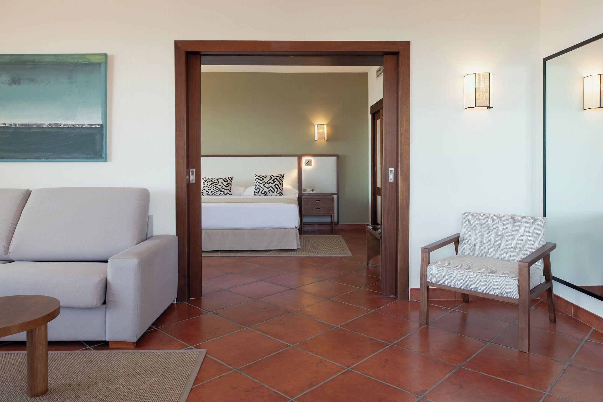A hotel room with a bed, a sofa, a chair, and a painting on the wall.