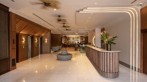 A modern lobby with a reception desk, seating area, and a bar in the background.