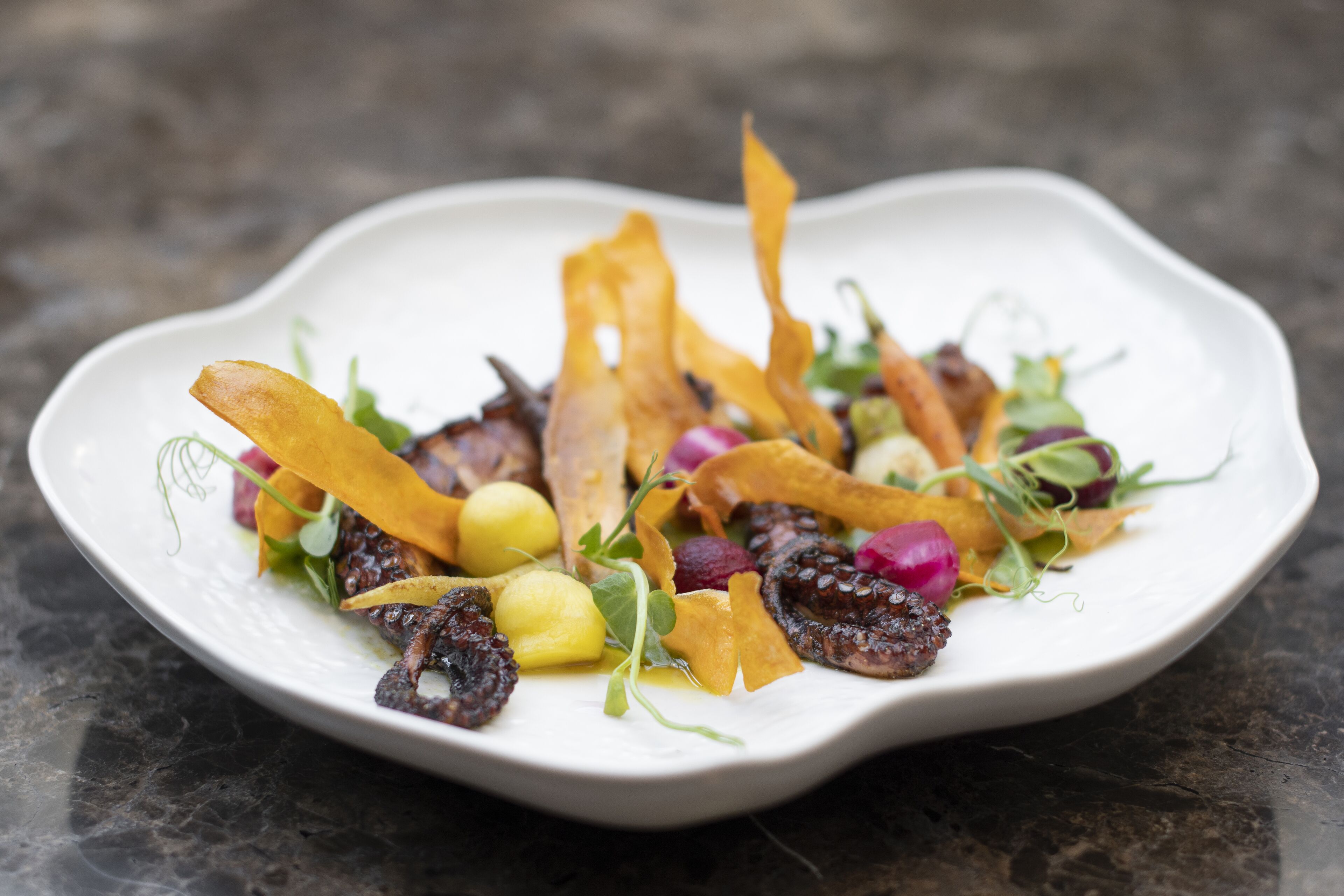 A white plate with a variety of food items including fruits, vegetables, and possibly some meat, arranged on a dark surface.