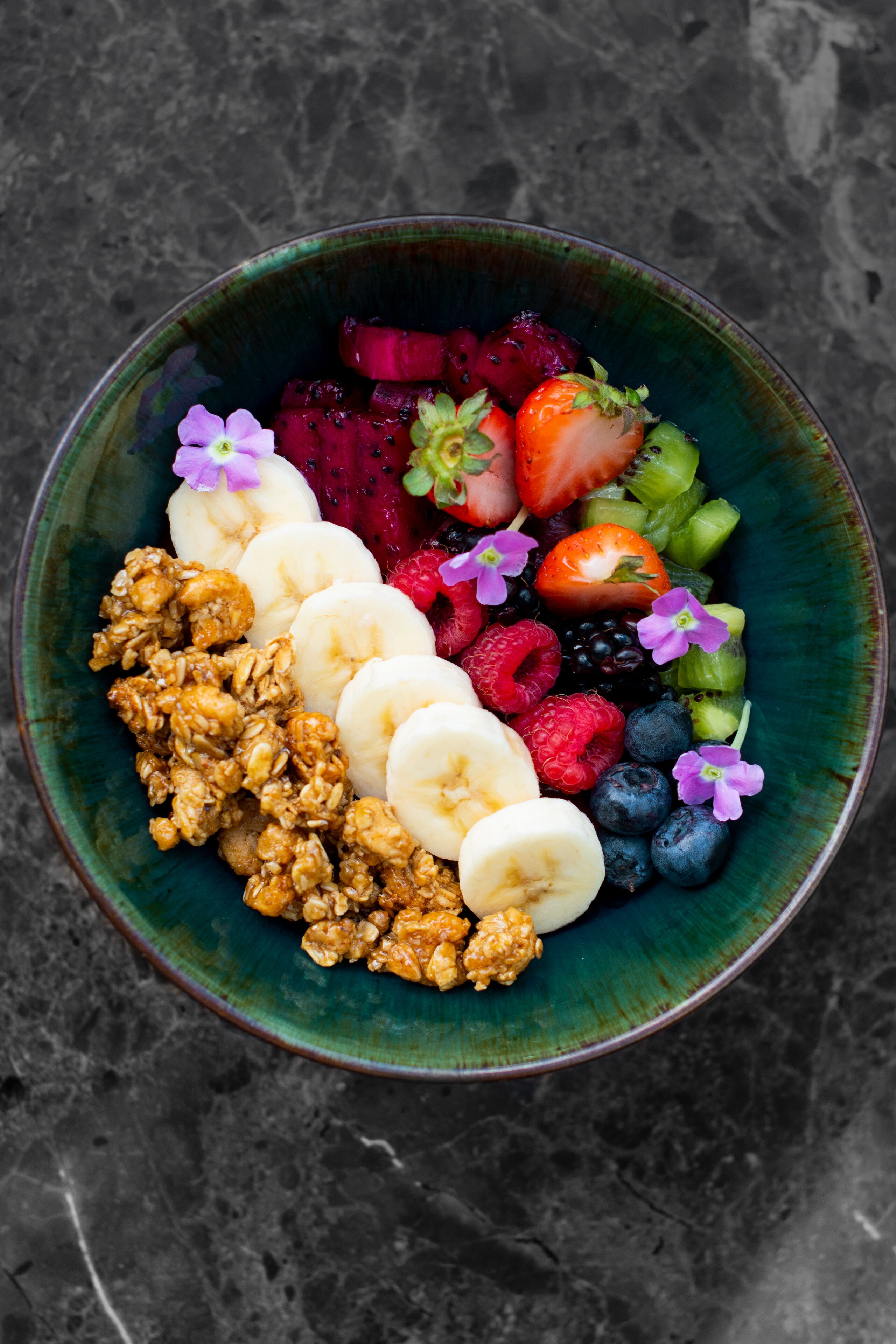 Un tazón de frutas variadas y granola sobre una superficie con textura.