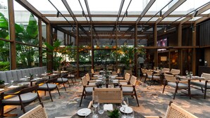 An indoor dining area with tables and chairs, a glass ceiling, and potted plants.