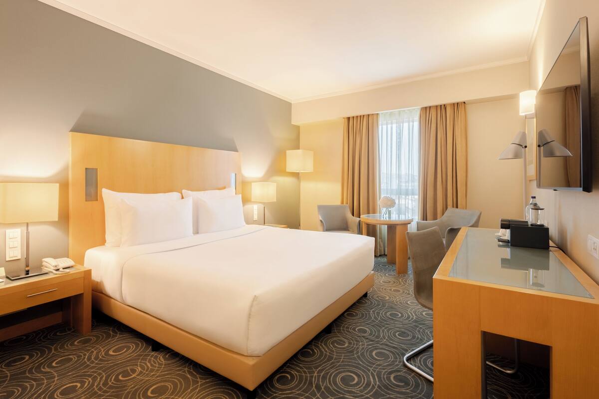 Ein Hotelzimmer mit einem großen Bett, Nachttischen, einem Schreibtisch, einem Sessel und einem Fernseher.