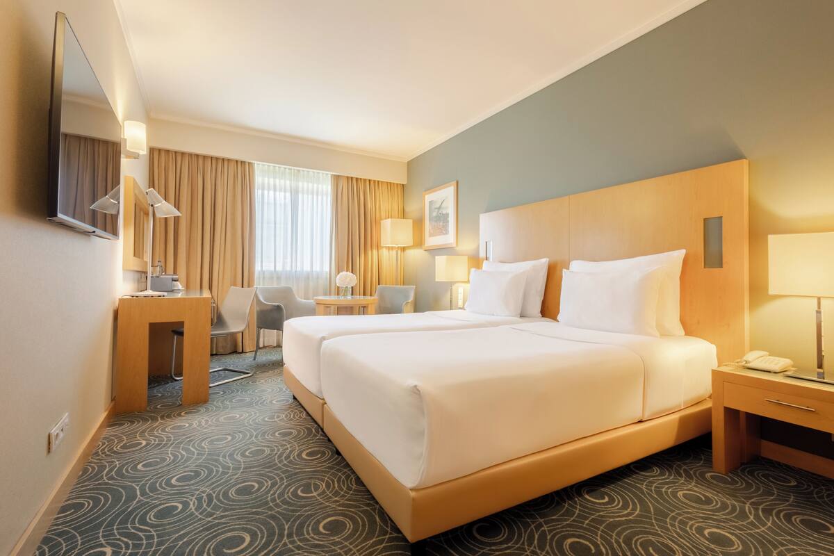 Ein Hotelzimmer mit einem großen Bett, einem Schreibtisch, einem Stuhl, einer Lampe und einem Fernseher.
