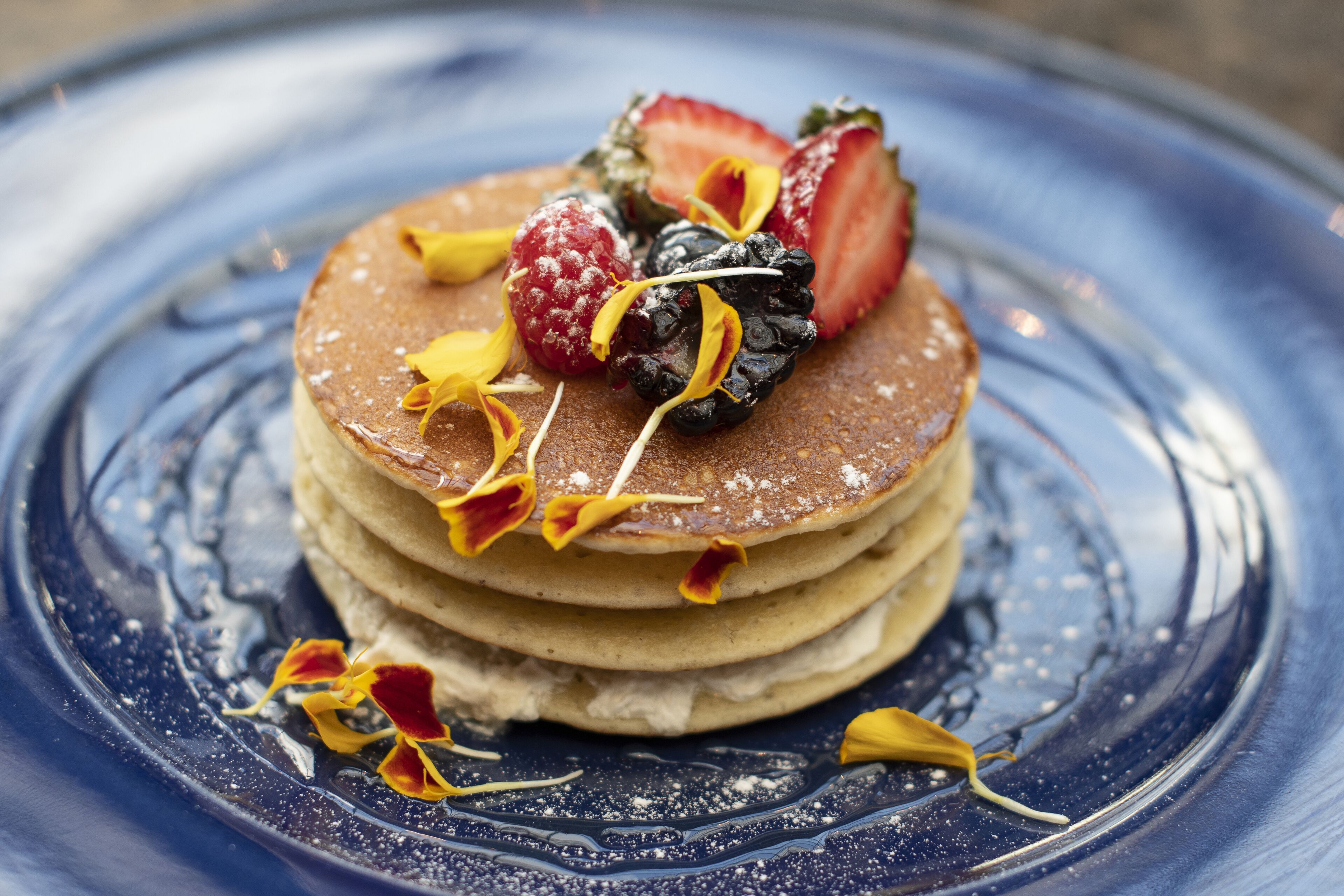 A stack of pancakes on a blue plate with strawberries and berries.