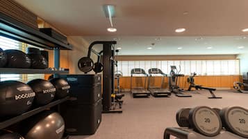 Un gimnasio con equipo de levantamiento de pesas, cintas de correr y un estante de mancuernas en la pared.