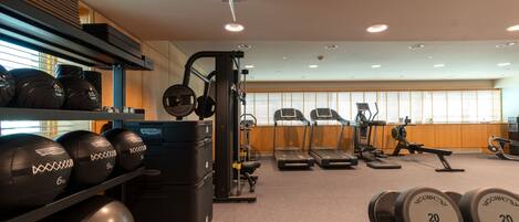 A gym with weightlifting equipment, treadmills, and a wall-mounted rack of dumbbells.