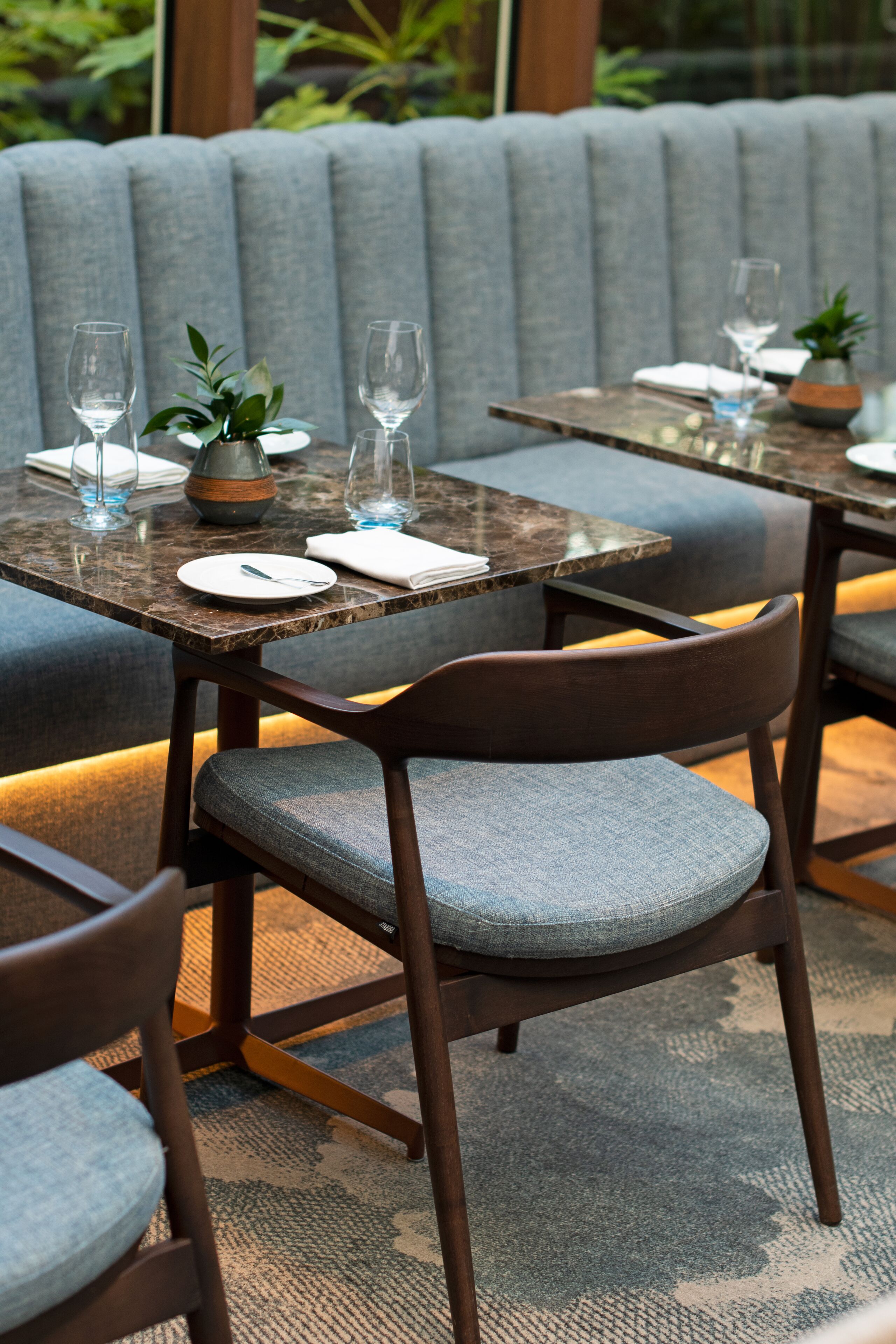 Uma área de refeições com mesa de mármore, cadeiras acolchoadas e um banco estofado cinza.