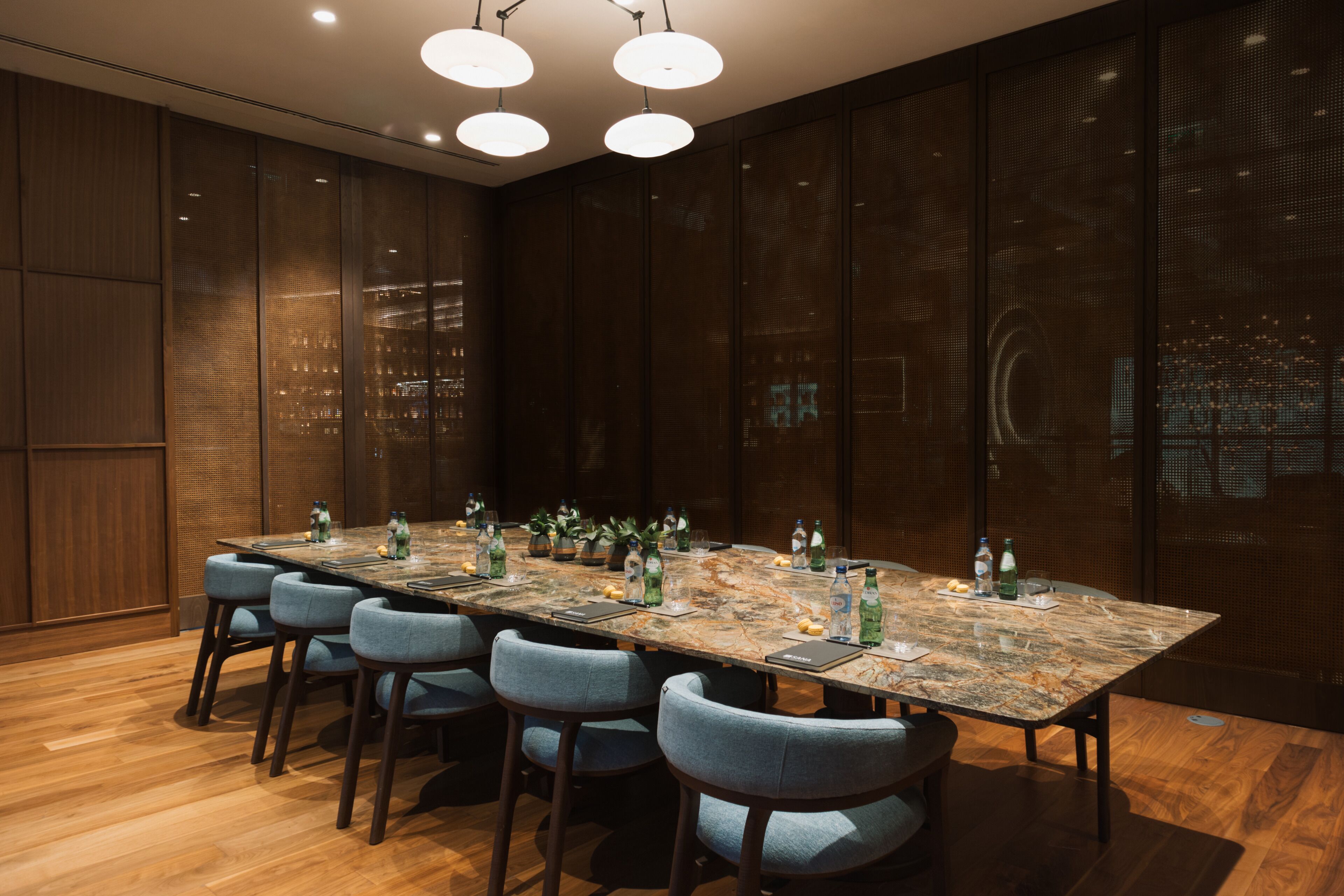 A conference room with a long table, six chairs, and a cityscape view through the glass wall.