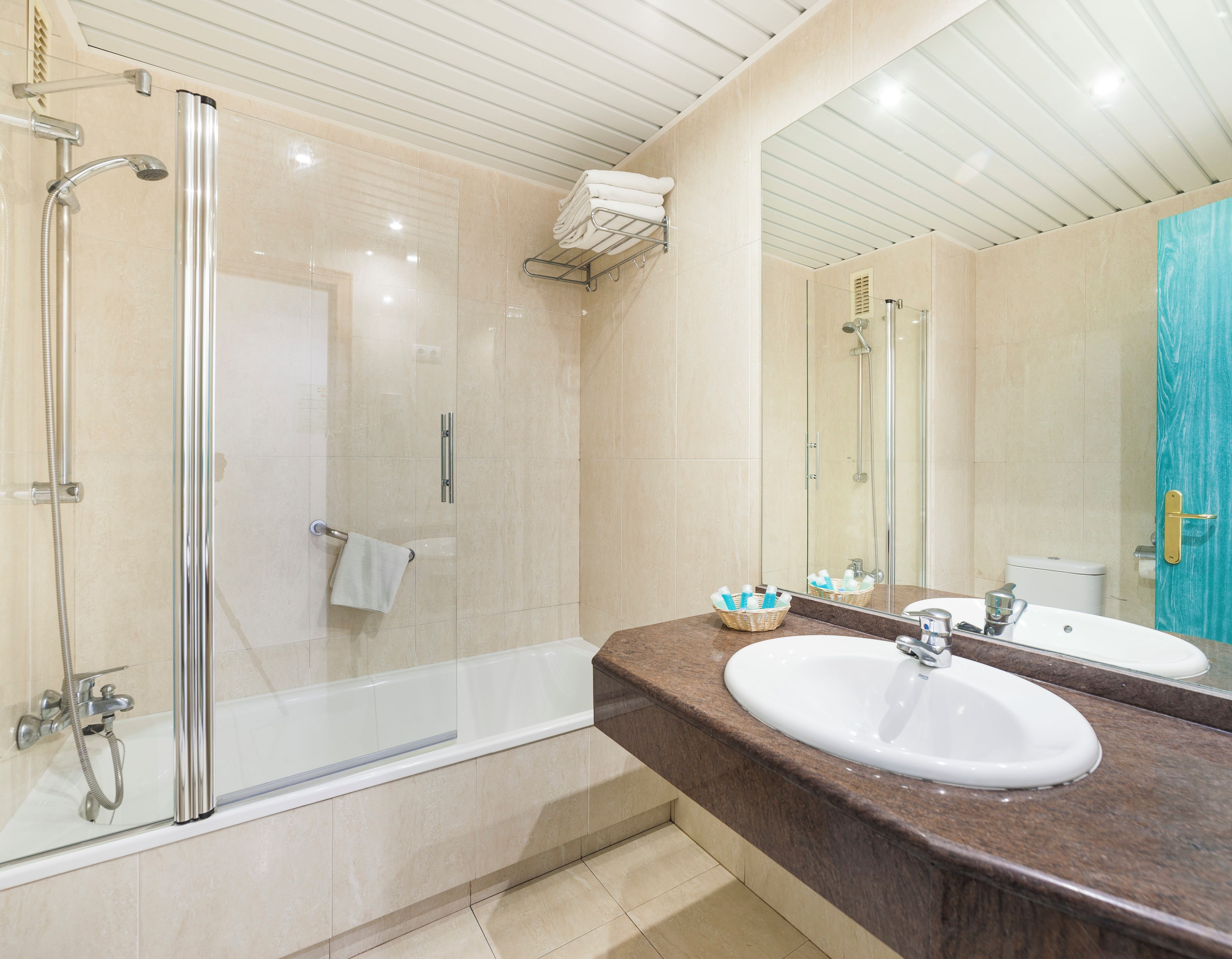 A modern bathroom with a glass-enclosed shower, a white bathtub, a marble countertop, and a large mirror.