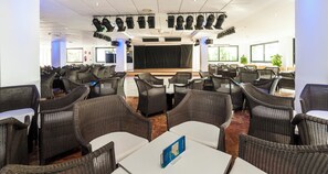 A conference room with a stage, multiple tables, and chairs arranged for an event. - Globales Los Patos Park (Benalmádena)