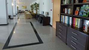 A hallway with a long, narrow carpet, a bookshelf filled with books, a desk with a computer, and a door marked "SIN SALIDA". - Globales Los Patos Park (Benalmádena)