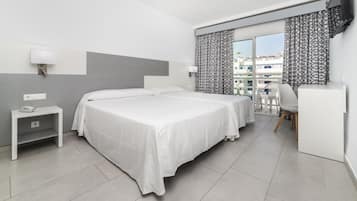 Habitación de hotel con dos camas, un escritorio, una silla y un balcón con cortinas estampadas.