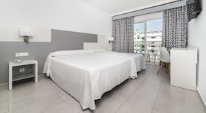 Een hotelkamer met twee bedden, een bureau, een stoel en een balkon met gordijnen met een patroon.