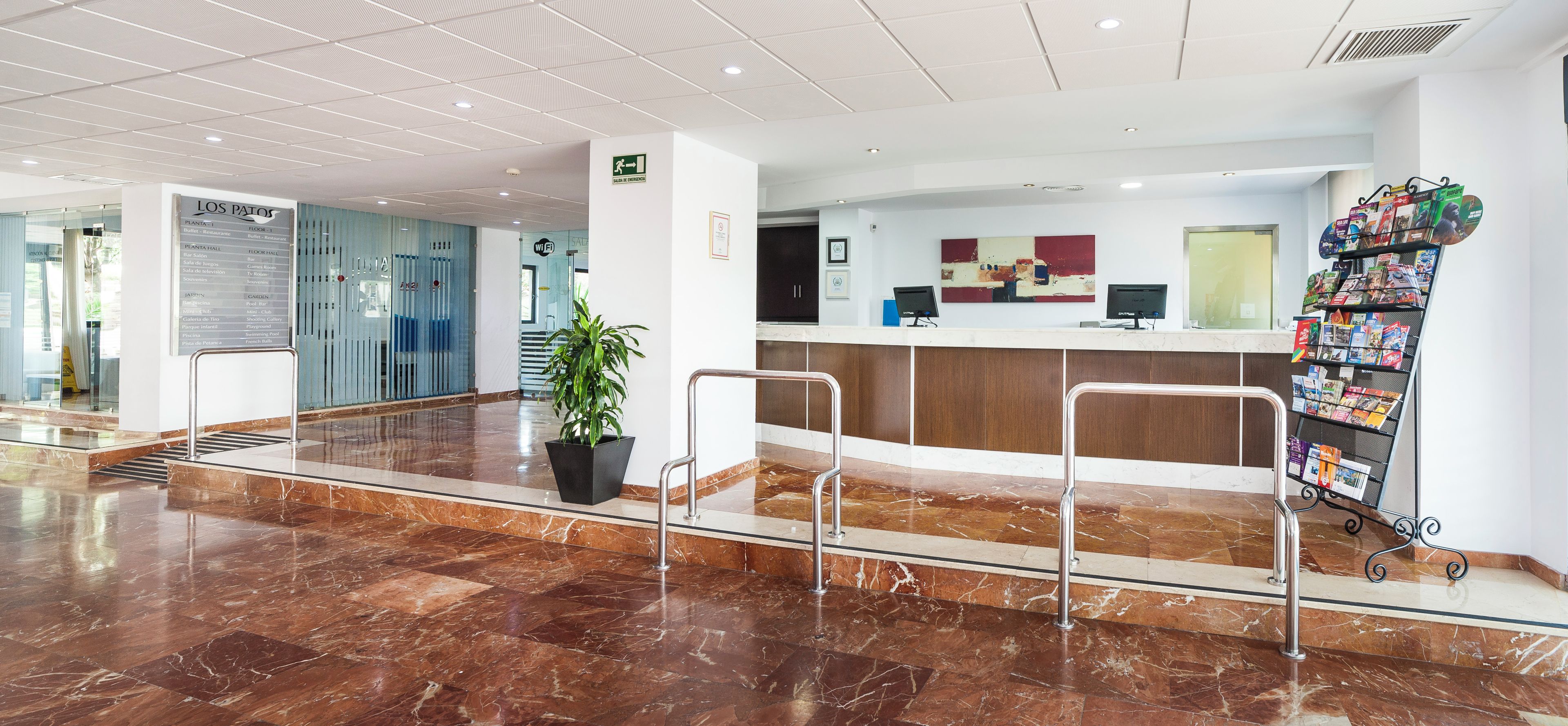 Un vestíbulo de hotel con una recepción, una planta y un atril para revistas.