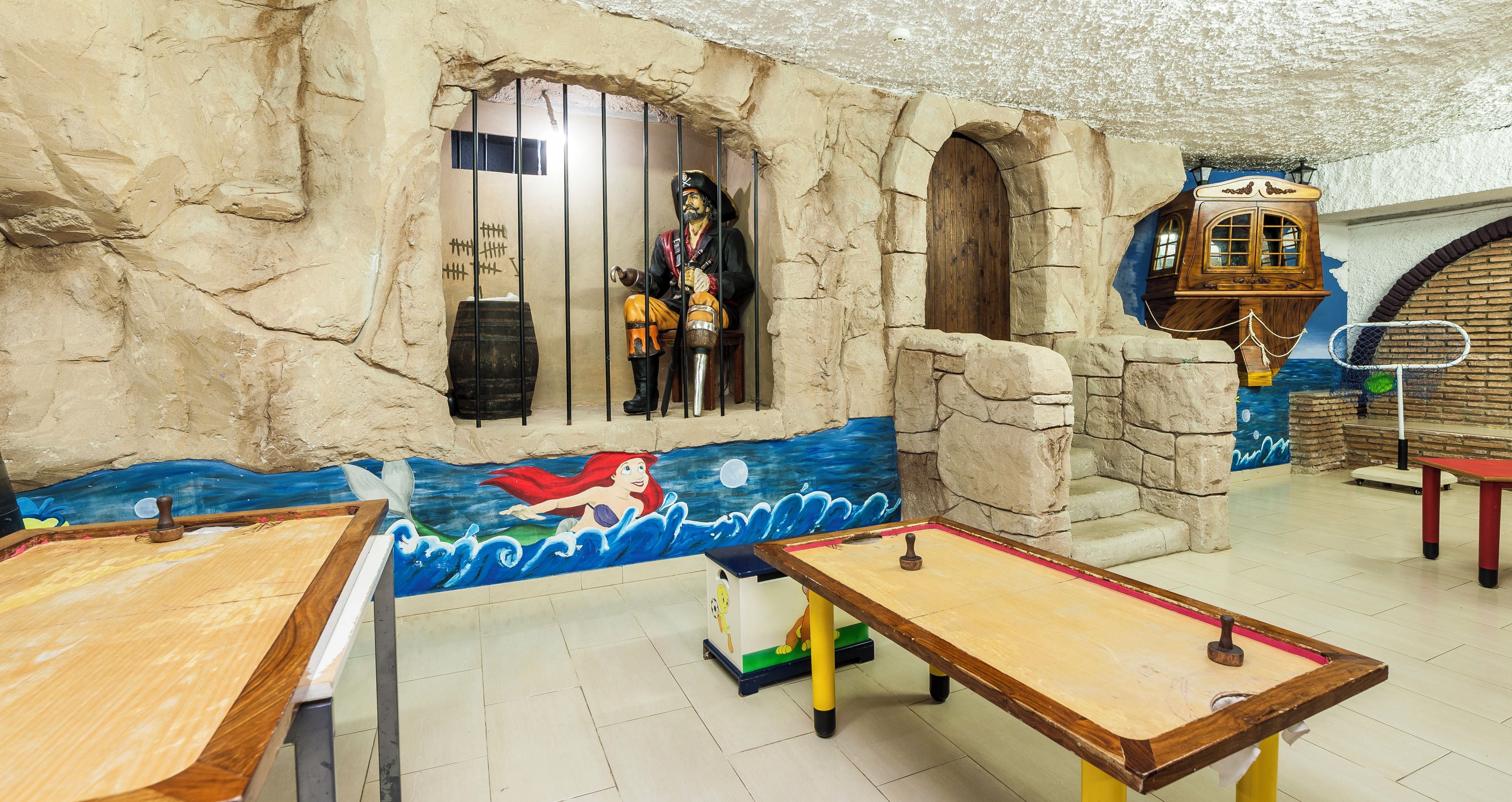Une pièce décorée d’une fresque représentant une sirène, avec un coffre en bois et une statue de pirate derrière des barreaux.