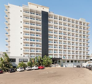 A multi-story hotel with a central tower, balconies, and a parking area.