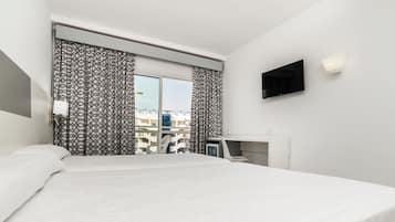 A modern hotel room with a large bed, a desk, a flat-screen TV, and a view of the city through the window.