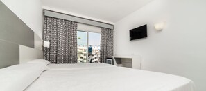 Une chambre d’hôtel moderne dotée d’un grand lit, d’un bureau, d’une télévision à écran plat et offrant une vue sur la ville par la fenêtre.