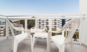 Un balcón con sillas de plástico blanco y una mesa, con vistas a una zona residencial con edificios de varios pisos.