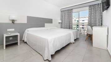 Una habitación de hotel con cama, mesita de noche, lámpara y vistas a edificios a través del ventanal.