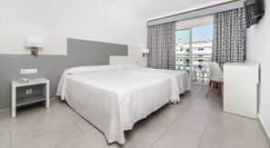 Une chambre d’hôtel avec un lit, une table de chevet, une lampe et une vue sur les bâtiments par la fenêtre.
