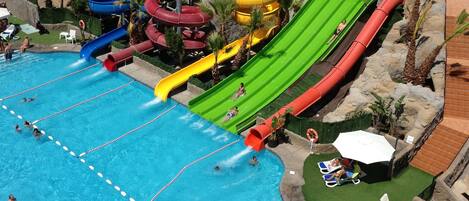 A swimming pool with multiple slides and a surrounding area with lounge chairs and umbrellas.