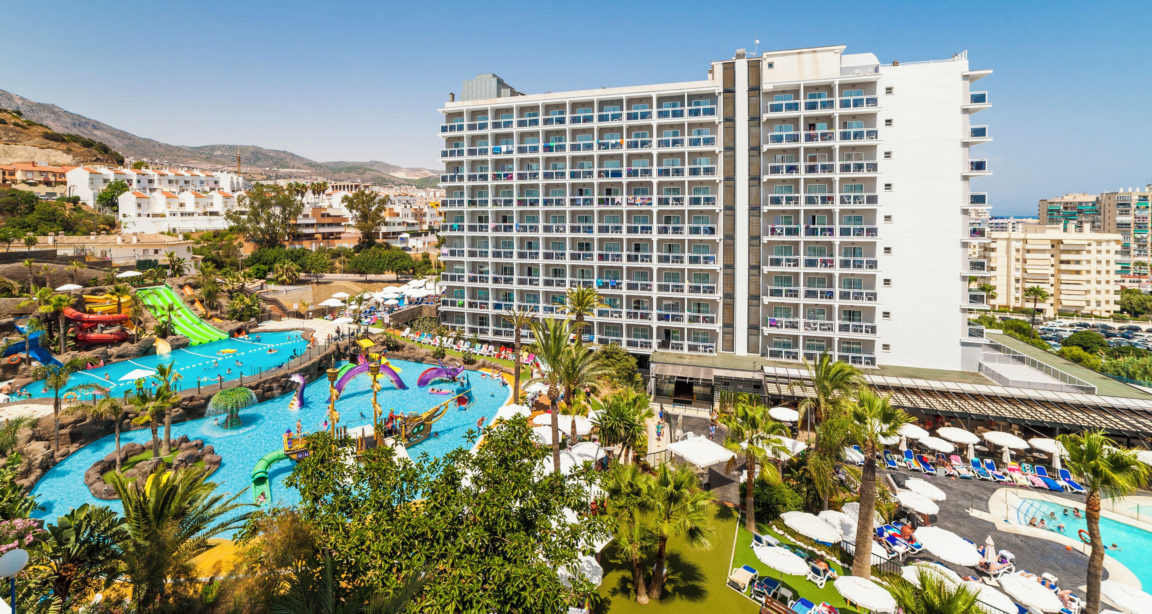 Un hotel con varios pisos, una piscina con toboganes y vistas del entorno.