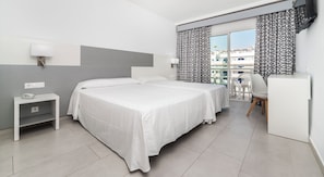 A hotel room with a bed, bedside table, lamp, and a view of buildings through the window.